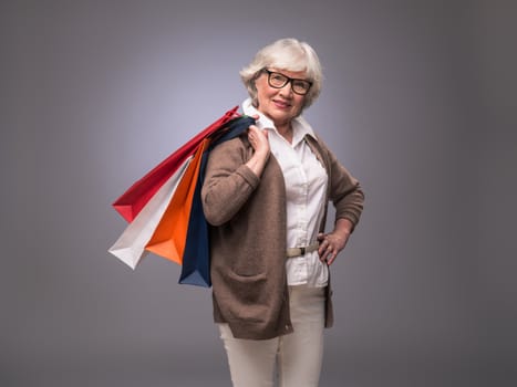 Studio portrait of happy senior woman with shopping bags