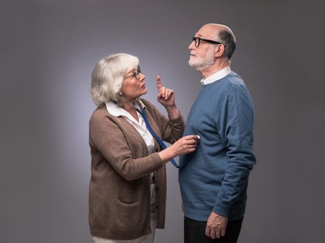 Old couple. Senior woman taking care, checking heart beat of husband with stethoscope