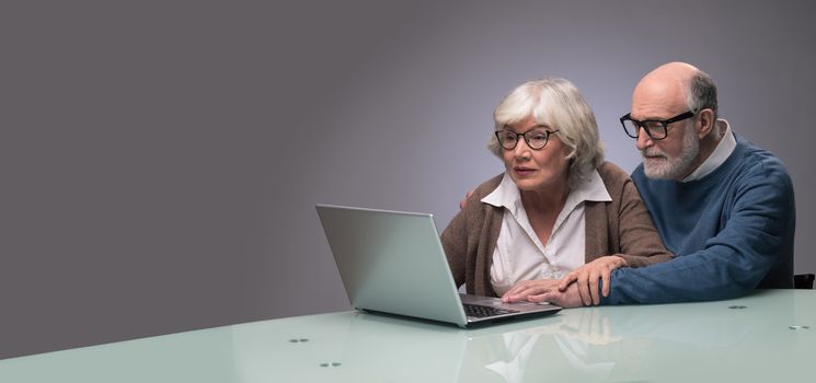 Ssenior couple looking at a laptop together, studio shot on gray background with copy space