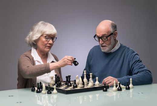 Elderly couple playing chess, studio shot on gray background