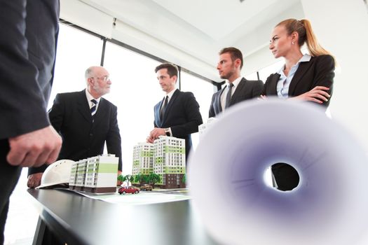 Business meeting of architects and investors looking at model of residential quarter houses and blueprints