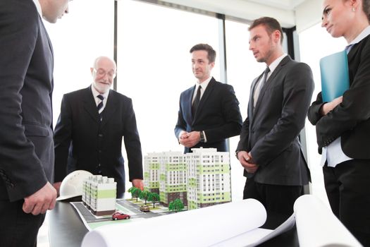 Business meeting of architects and investors looking at model of residential quarter houses and blueprints