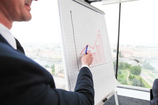 Serious confident business coach gives presentation on flipchart training , executive presenter team leader explaining graph on whiteboard at corporate meeting