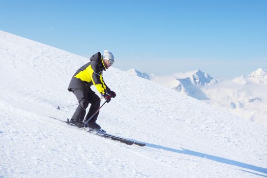 Alpine skier on piste running downhill in beautiful Alpine landscape. Blue sky on background. Free copy space for text