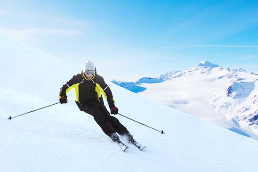 Alpine skier on piste running downhill in beautiful Alpine landscape. Blue sky on background. Free copy space for text