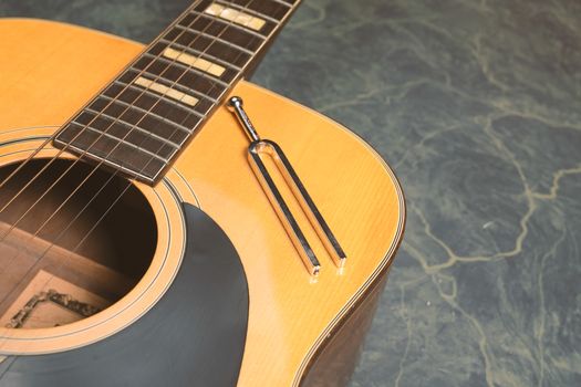 Acoustic guitar on a green marble background, on the guitar there is a tuning fork, music concept.