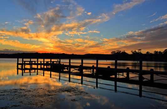 Beautiful sunset and mirrored reflections against a timber jetty silhouette