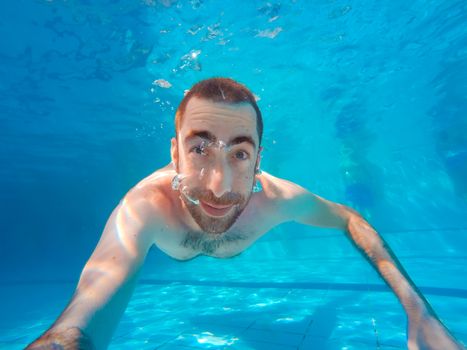 Young handsome man diving underwater in a swimming pool.