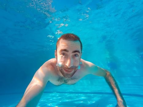 Young handsome man diving underwater in a swimming pool.