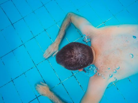 Top view of a young handsome man diving underwater in a swimming pool.