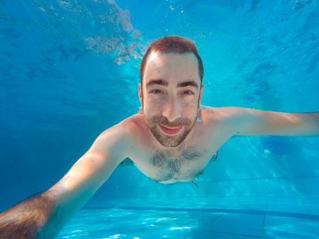 Young handsome man diving underwater in a swimming pool. He smiling and looking at camera.