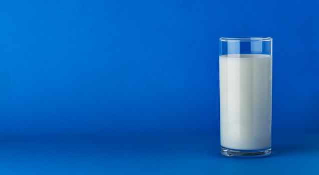Glass of fresh milk isolated on blue background with copy space