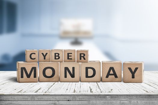 Cyber monday sign on a wooden desk with a monitor in a blue room in the background