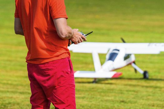 Man flying a model airplane with a controller on a green lawn in the summer