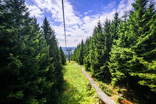 Mountain lift in the summer with pine trees up the hill under a blue sky