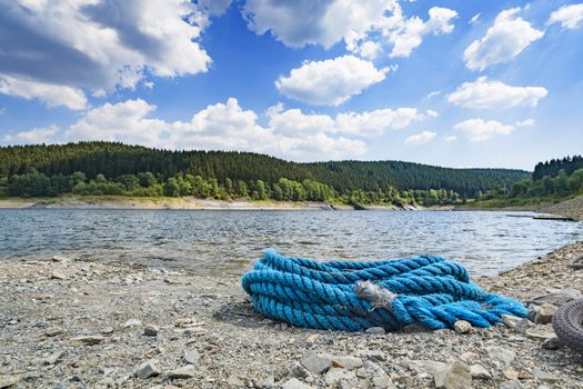 Blue rope on a pebble beach in the summer with a large green forest in the background