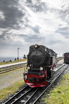 Black locomotive with red color driving on a railtrack under a cloudy sky