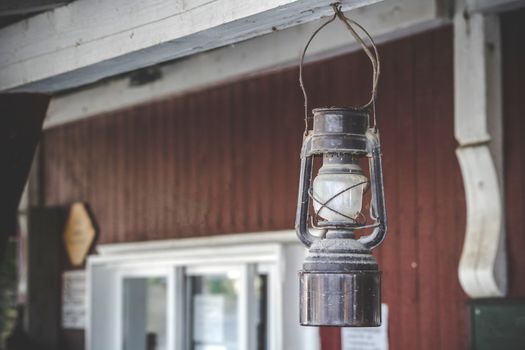 Old oil lamp hanging on a porch outside a red house in old style