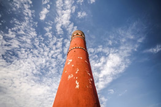 Tall red chimney tower under a blue sky with white clouds