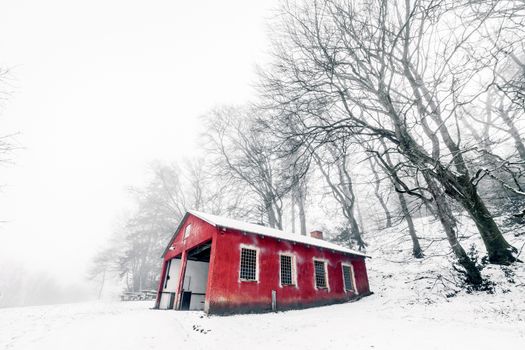 Red barn in a misty winter landscape with barenaked trees in the foggy weather