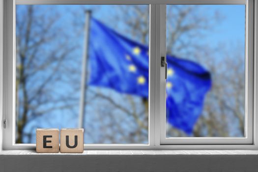 EU sign in a window with the European union flag outside waving in the wind