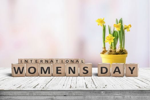 International Womens day sign with a yellow daffodil flower on a wooden desk with a pink background