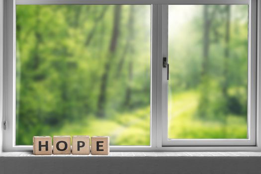 Hope sign in a window sill with a view to a green forest in sunlight