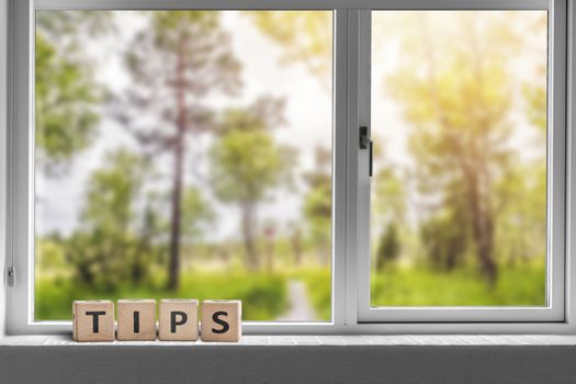 Tips sign in a window with a view to a green garden with tall trees in sunlight