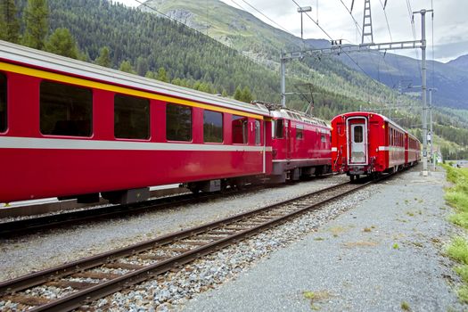 The train pulls up to the station of the old narrow-gauge railway in the valley of the Alpine mountains among the trees in cloudy weather.