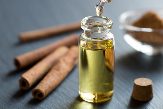 A drop of cinnamon essential oil is being dropped into a bottle, with cinnamon sticks and powder in the background