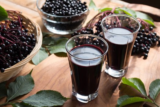 Two glasses of elderberry syrup, with fresh elderberries in the background
