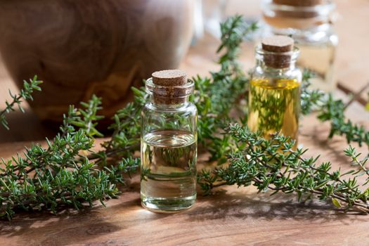 A bottle of thyme essential oil with fresh thyme twigs and other bottles in the background