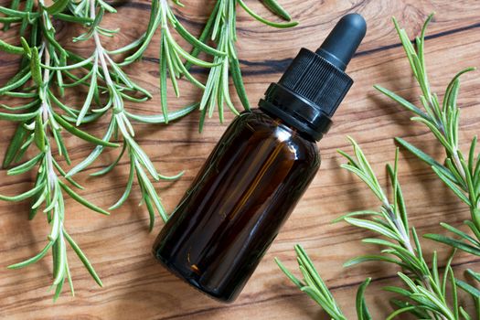 A bottle of rosemary essential oil with fresh rosemary twigs on a wooden background