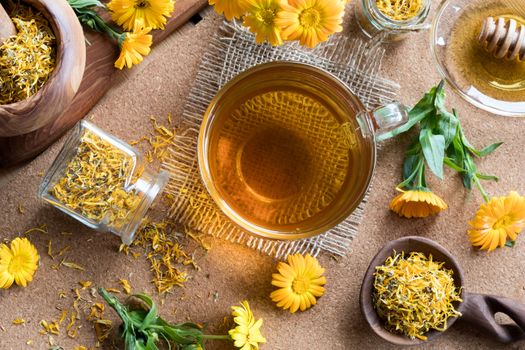 A cup of calendula (marigold) tea on a table, with fresh and dry calendula flowers in the background, top view