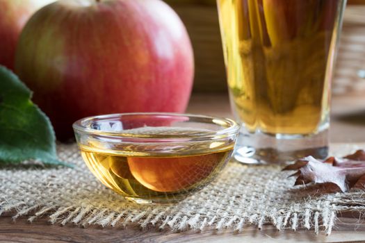 Apple cider vinegar in a glass bowl, with apples and leaves in the background