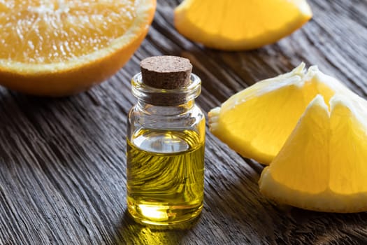 A bottle of orange essential oil on old wood, with fresh oranges in the background