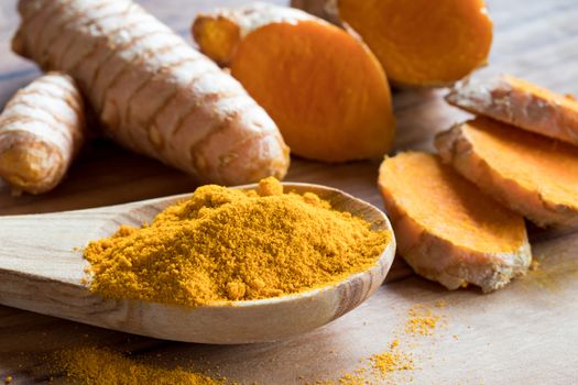 Turmeric powder on a wooden spoon, with fresh turmeric root in the background