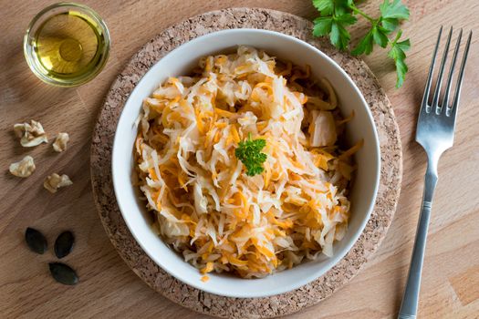 Fermented cabbage and carrots in a bowl on a wooden table, top view