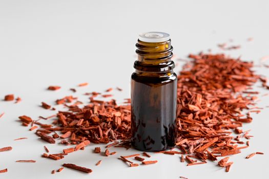 A bottle of sandalwood essential oil with sandalwood on a white background