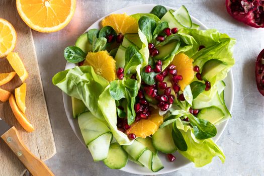 Fruit and vegetable salad on a bright metal background, top view. Lettuce, corn salad, cucumber, avocado, orange, pomegranate.