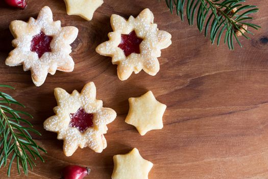 Christmas background with star-shaped Linzer Christmas cookies with strawberry jam, dried rose hips and spruce branches