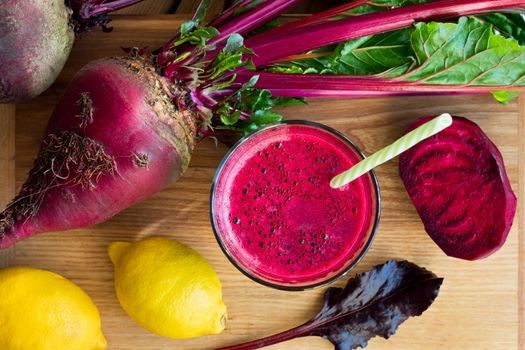 Red beet juice in a glass on a wooden table with whole beets and lemons, top view