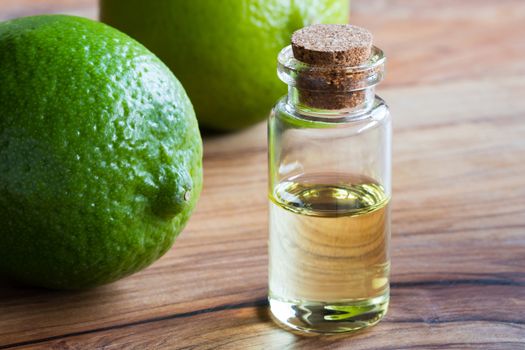 A bottle of lime essential oil on a wooden table, with fresh limes in the background