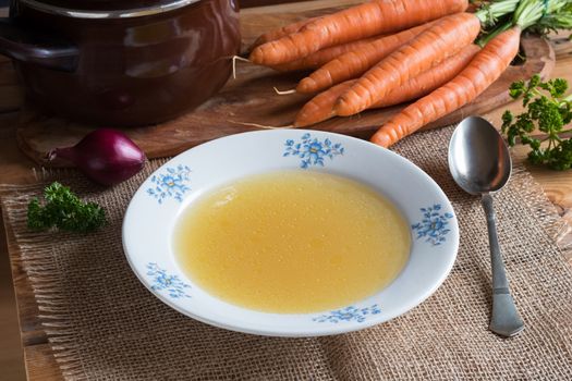 Chicken stock in a plate on a wooden table, with vegetables in the background