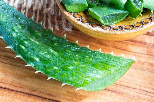 Aloe vera leaf on a wooden table with sliced aloe vera in the background