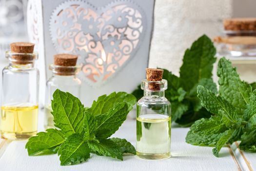 A bottle of essential oil with fresh peppermint leaves on white wooden background