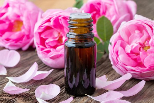 A bottle of essential oil with roses on a wooden background