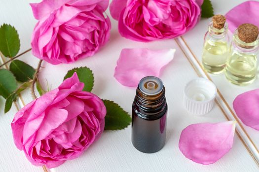 A bottle of essential oil with fresh roses on a white table