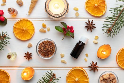 Bottles of essential oil on a white Christmas background with frankincense, myrrh, dried orange slices and candles made from nut shells