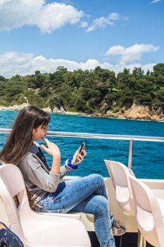Teen girl enjoys spring vacation in a sea voyage on a pleasure boat. She sits on the upper deck communicates by video call.